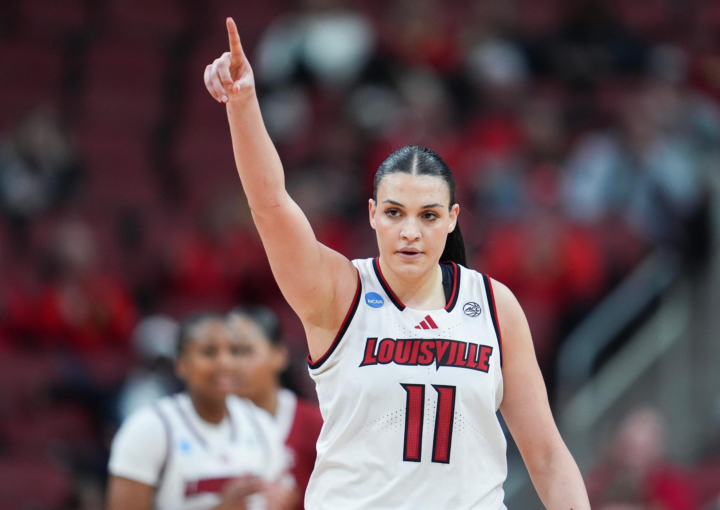 A women's basketball player points her finger up in the air.